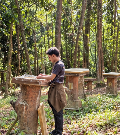 A beekeeper tending a hive box on a carved log stand among tall trees.